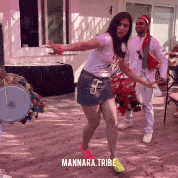 a woman in a short skirt is dancing in front of a man playing drums and a sign that says mannara tribe