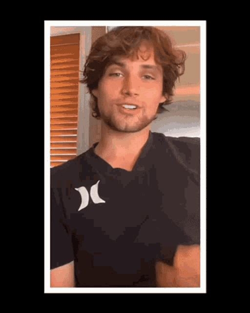 a young man with a beard wearing a black hurley t-shirt .