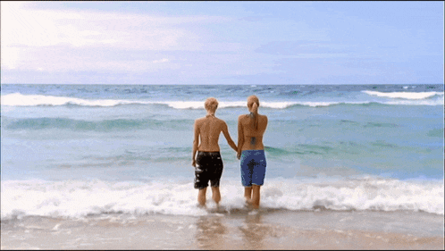 a man and a woman are walking into the ocean