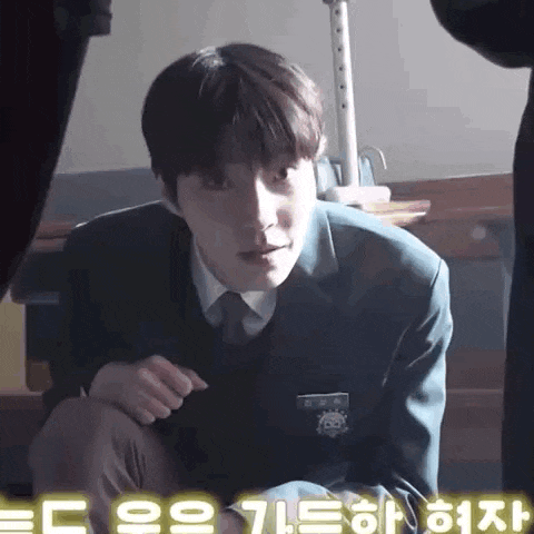 a young man in a suit and tie is kneeling down in a classroom .