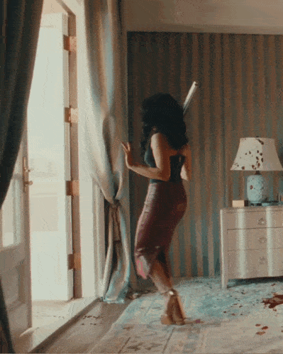a woman is standing in a room with a lamp on the nightstand
