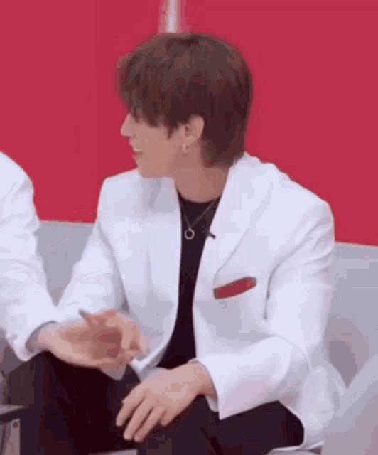 a man in a white jacket and black pants is sitting on a couch and talking to another man .