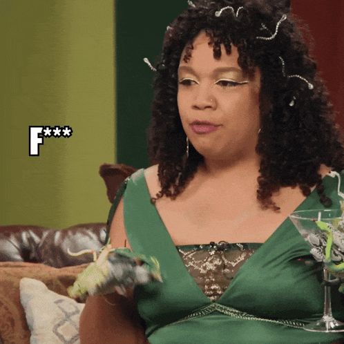 a woman in a green dress is sitting on a couch with a martini glass in front of her and the letter f is above her head