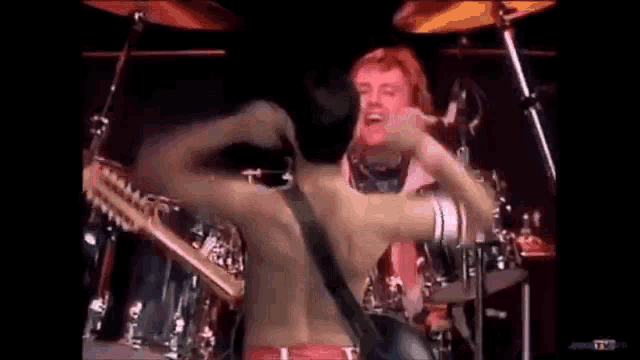 a man without a shirt is playing a guitar and singing on a stage .