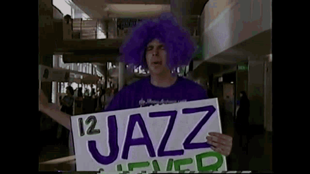 a man wearing a purple wig is holding a sign that says 12 jazz lever