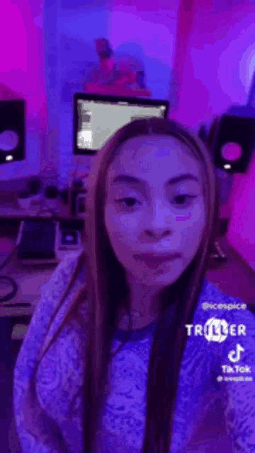 a girl is standing in a room with purple lights and a computer .