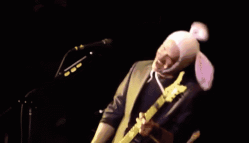 a man wearing a pink bunny hat is playing a guitar on stage .