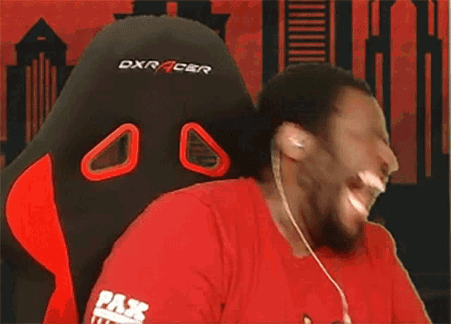 a man in a red shirt is sitting in a dxracer chair