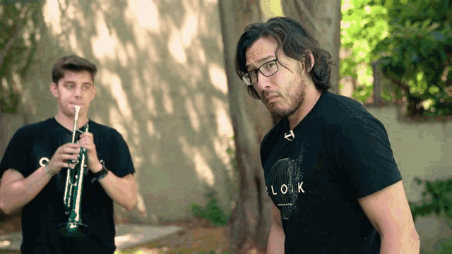 a man wearing a black shirt that says look looks at another man playing a trumpet
