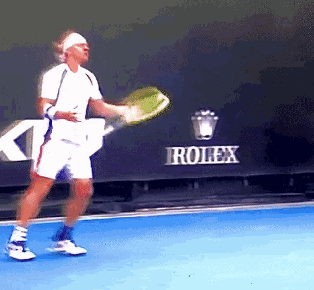 a man holding a tennis racquet in front of a rolex sign