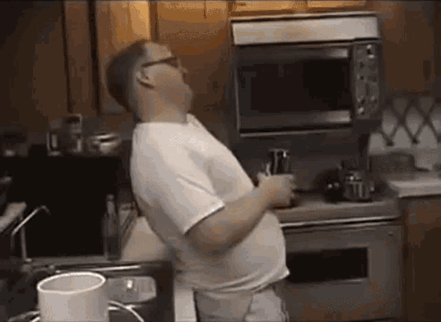 a man in a white shirt is standing in a kitchen with a microwave .