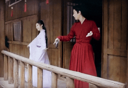 a man in a red dress is standing next to a woman in a white dress on a balcony .