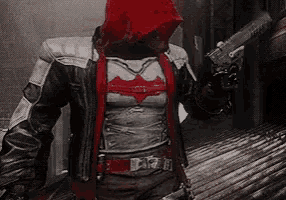 a man in a red hood is holding a gun in a dark room .
