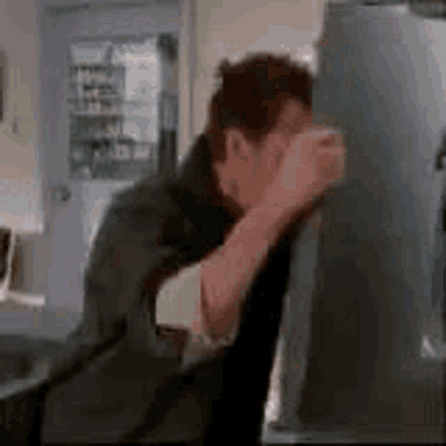 a man is standing in front of a refrigerator with his head in his hands .