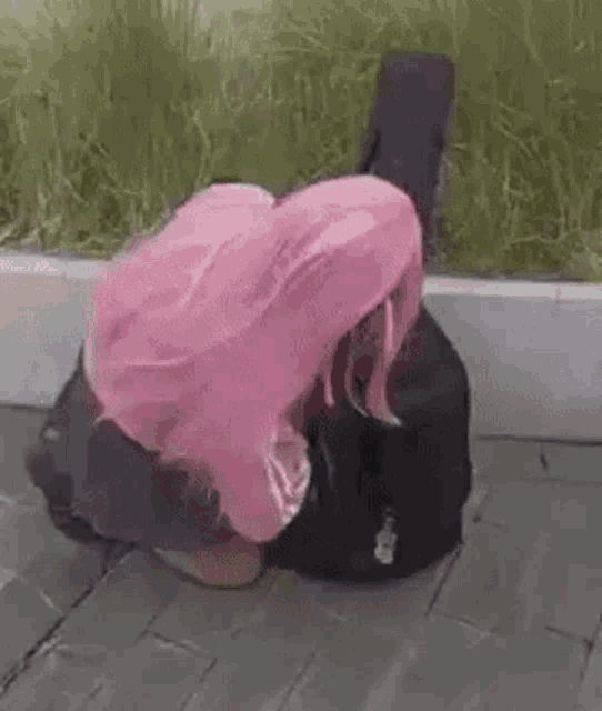 a girl with pink hair is kneeling down next to a guitar case on the sidewalk .