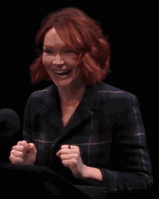 a woman with red hair is laughing while sitting at a podium in front of a microphone