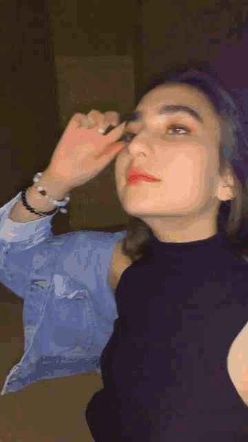 a woman wearing a denim jacket and a black turtleneck applying makeup