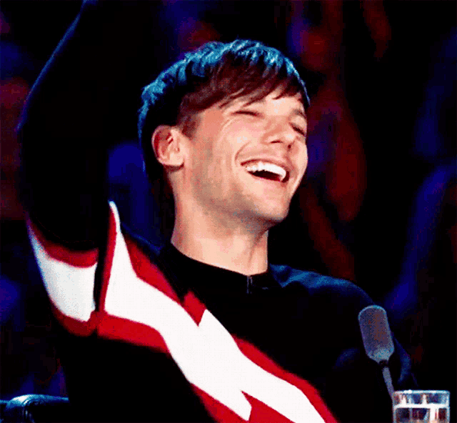 a man is sitting in front of a microphone with his arms in the air and laughing .