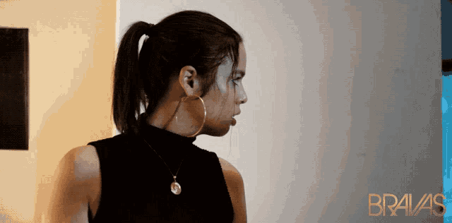 a woman wearing hoop earrings is standing in front of a wall that says bravas