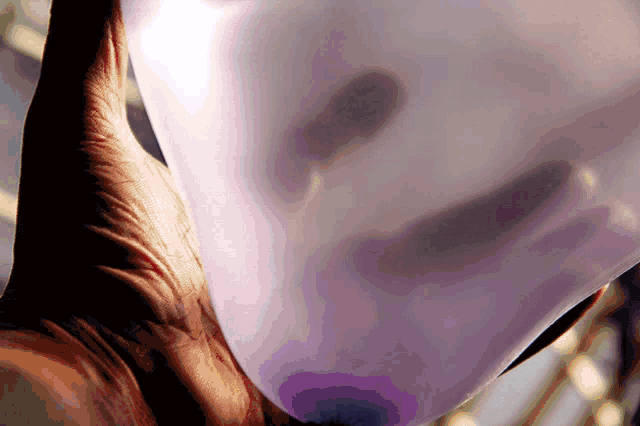a hand is holding a purple balloon that looks like a mask