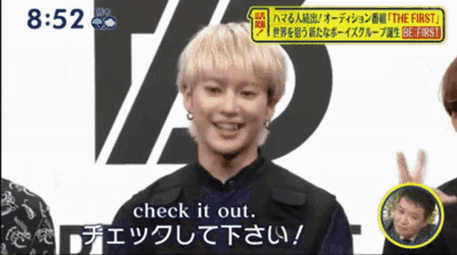 a man with blonde hair is smiling in front of a sign that says the first
