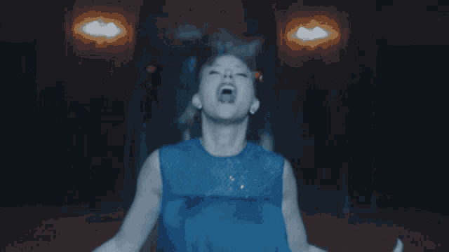 a woman in a blue dress with red lipstick stands in a dark room