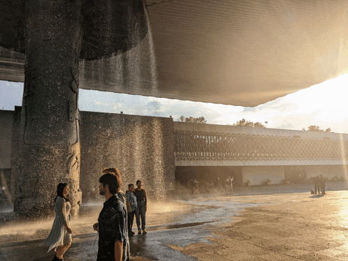 a group of people standing under a waterfall in front of a large building