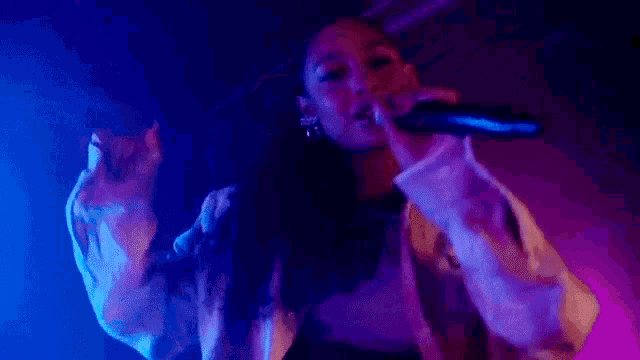 a woman is singing into a microphone in front of a purple and blue light .