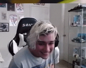 a man with blonde hair is sitting in a gaming chair and smiling in a room .