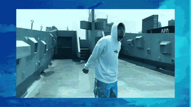 a man in a white hoodie stands on a rooftop in front of a building that says apa