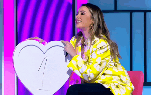 a woman in a yellow jacket is holding a white heart with the letter n on it .