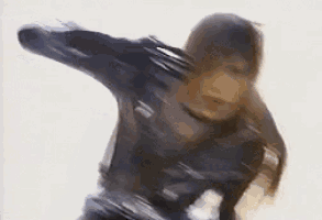 a woman in a leather jacket is holding a gun in her hand and dancing .