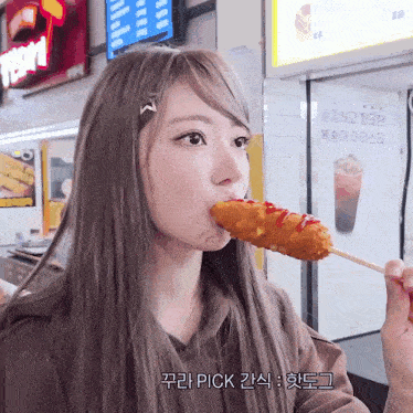 a girl is eating a fried food on a stick with a sign in the background that says pick