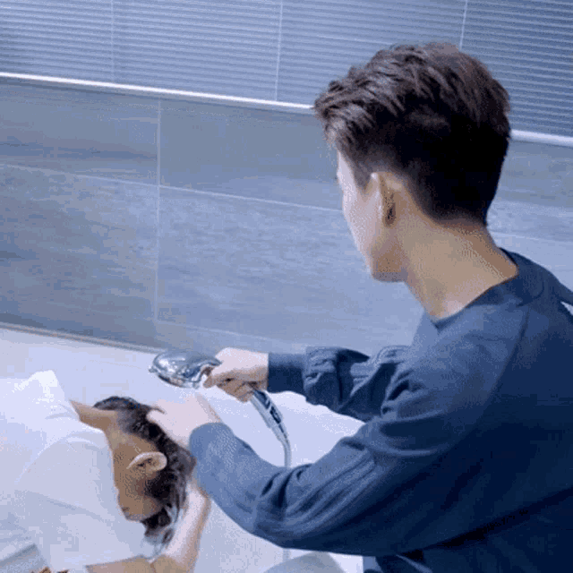 a man is washing another man 's hair in a bathroom .