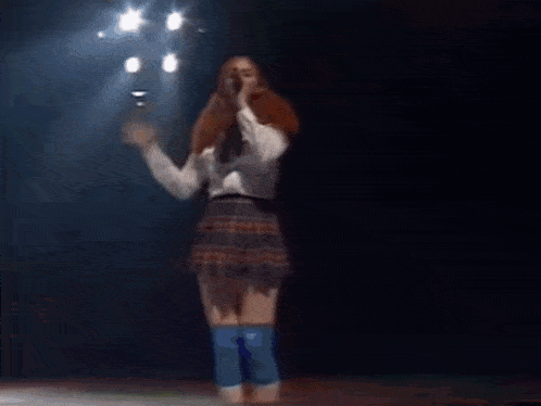 a woman with red hair is singing into a microphone while dancing on a stage .