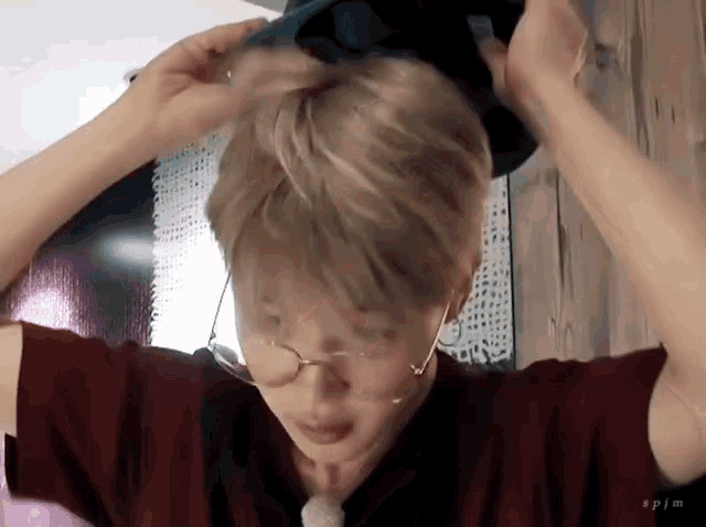 a man wearing glasses and a red shirt is putting a hat in his hair .