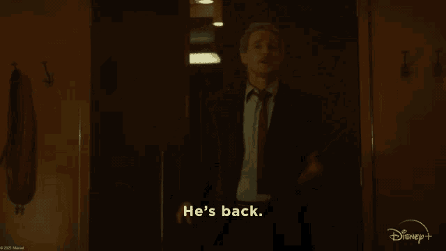 a man in a suit and tie is standing in a doorway and saying he 's back