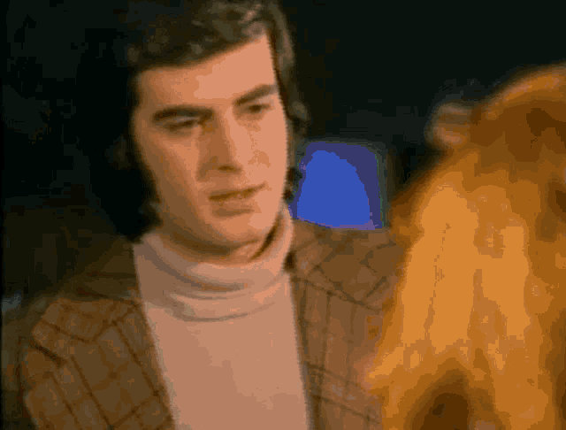 a man in a plaid jacket and a white turtleneck is looking at a woman