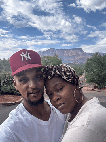 a man wearing a ny hat stands next to a woman wearing hoop earrings