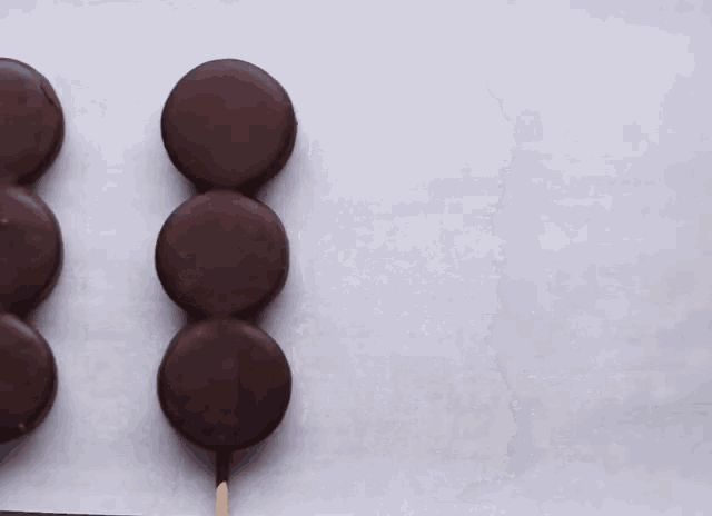 three chocolate covered cookies are on sticks on a white surface