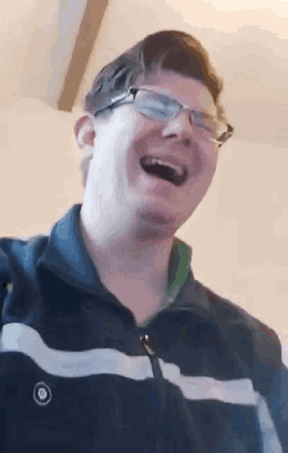 a man wearing glasses is laughing with his mouth open .