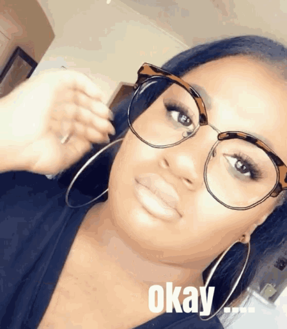 a woman wearing glasses and hoop earrings says okay on the bottom of her face