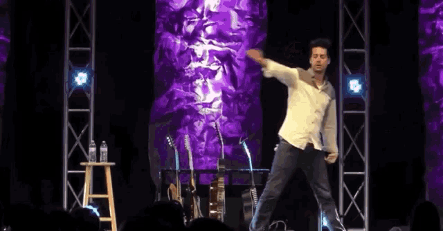 a man stands on a stage with his arms outstretched in front of a purple background