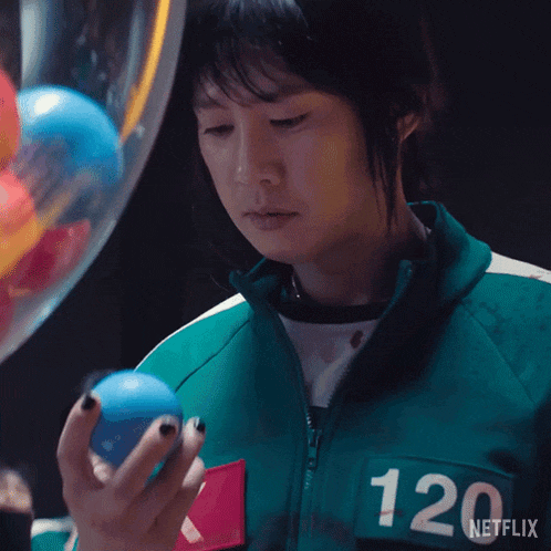 a woman in a green jacket with the number 120 on the back is holding a blue ball .