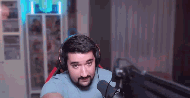 a man with a beard wearing headphones and a microphone is sitting in front of a computer monitor .
