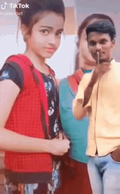 a girl in a red vest is standing next to a man in a yellow shirt and a woman in a blue shirt .