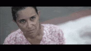 a woman in a pink shirt is looking at the camera with a sad look on her face .