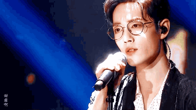 a young man wearing glasses is singing into a microphone on a stage