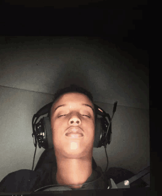 a young man wearing headphones with his eyes closed looks at the camera