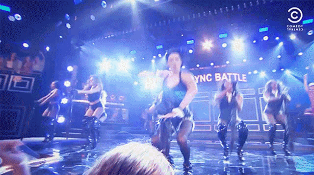 a group of women are dancing on a stage with sync battle written on the wall behind them